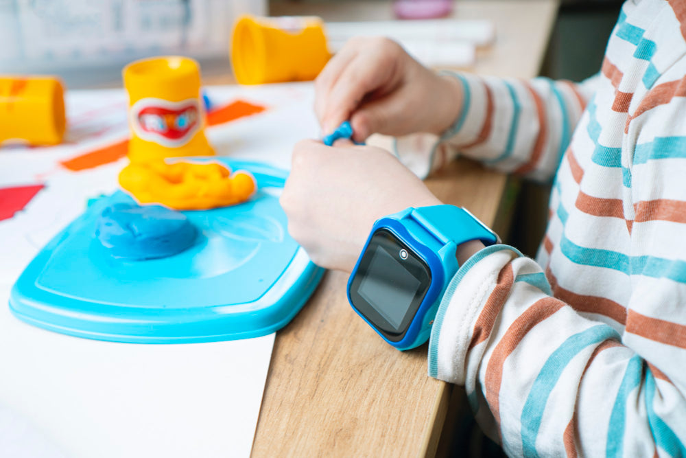 Een kinder smartwatch om de pols van een kind. Het heeft een kleurrijk scherm, knoppen aan de zijkant en functies zoals een stappenteller, GPS-tracking, spelletjes en een camera